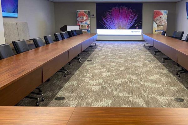Another angle of the same conference space, showing a long rectangular setup of tables and chairs facing a large display. Colorful posters featuring children’s photos decorate the room, indicating a family- or child-oriented theme.