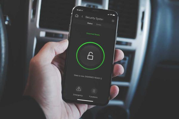 A stylish bedroom with a coffered ceiling, featuring a modern fireplace beneath a wall-mounted TV. A white upholstered bed faces the fireplace, and an arched mirror leans against the wall, adding an elegant touch.